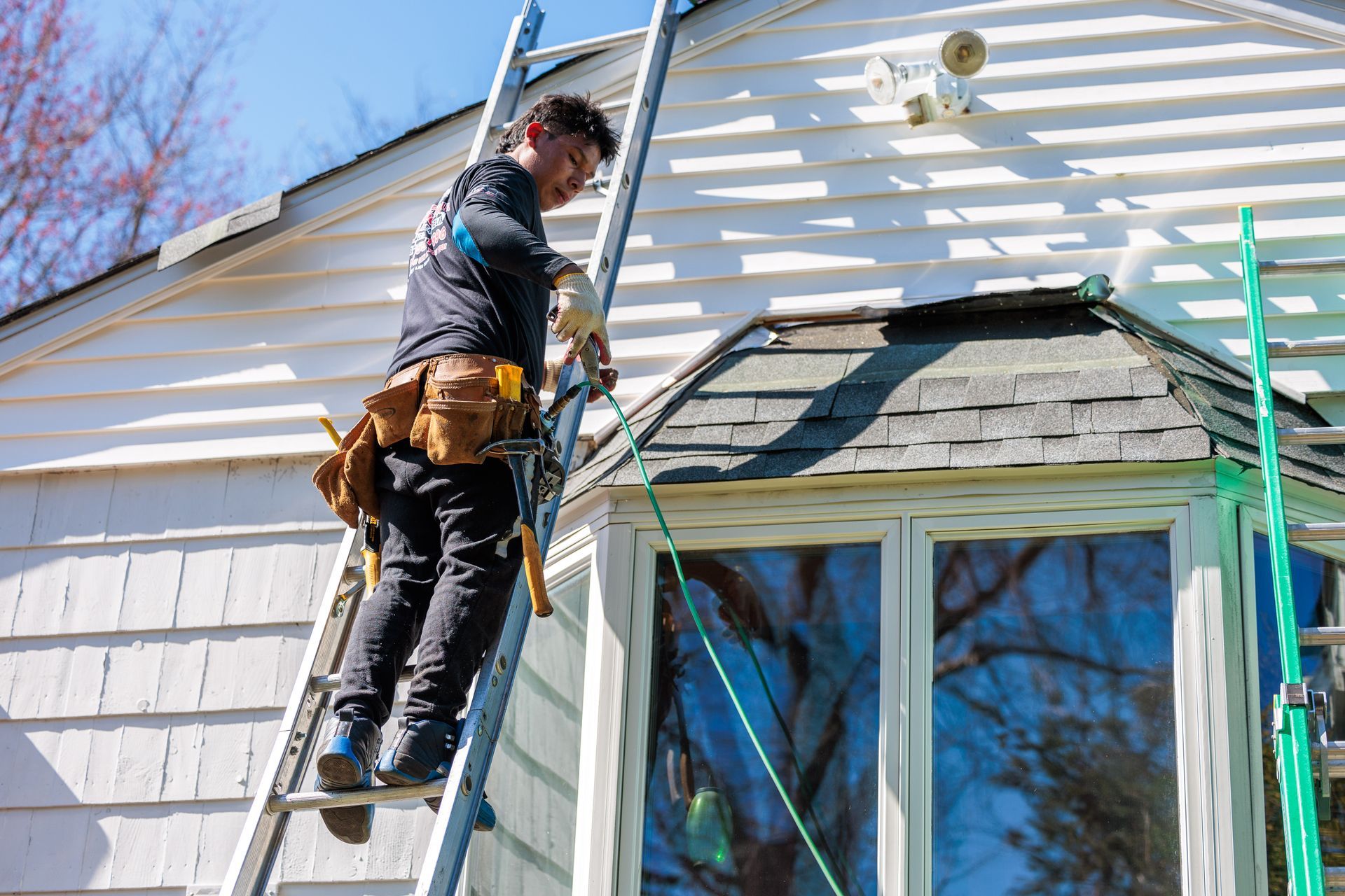 Worker on a ladder repairing a house roof beside a window