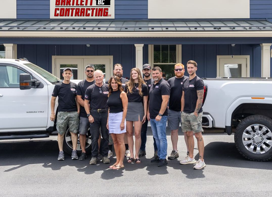 Group of people posing in front of white trucks outside a contractor business building.