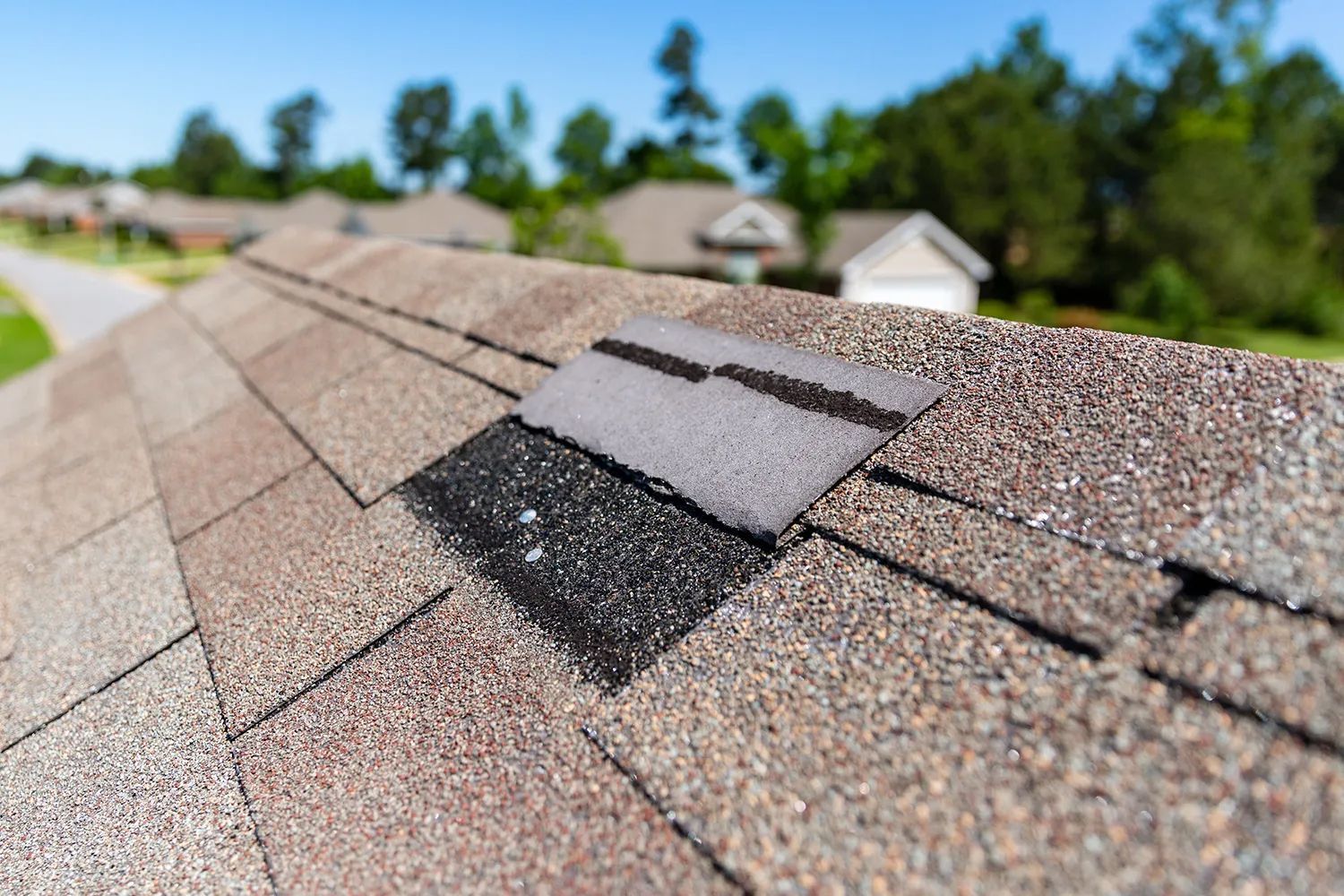 Damaged asphalt roof shingles with torn and missing sections on a suburban house