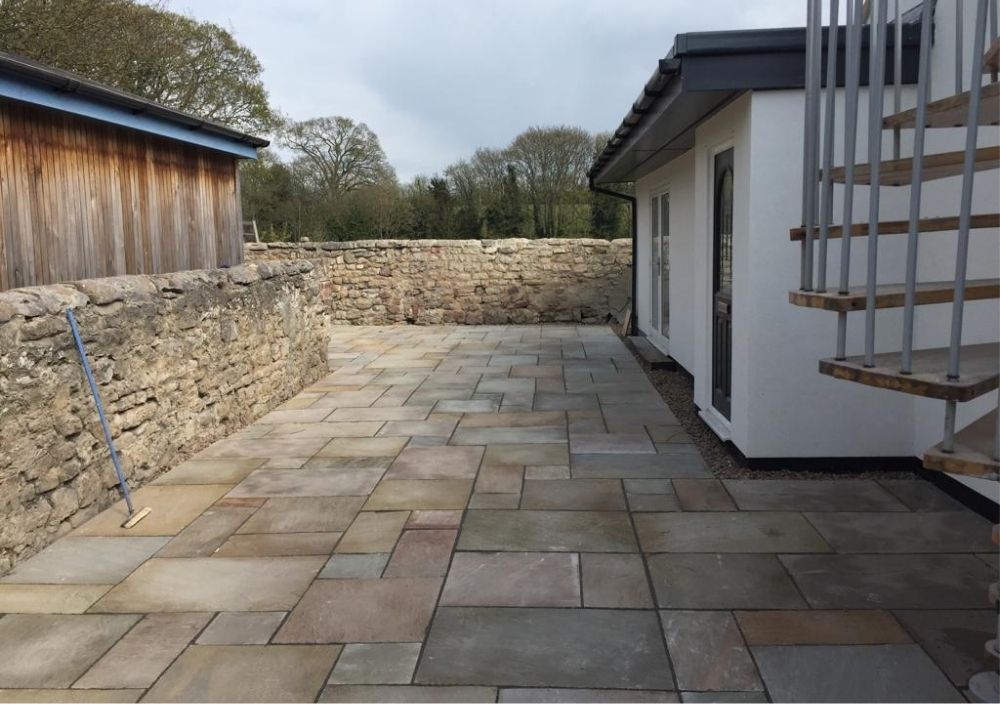 Natural stone patio running alongside a garden building with a stone wall behind in Headingley