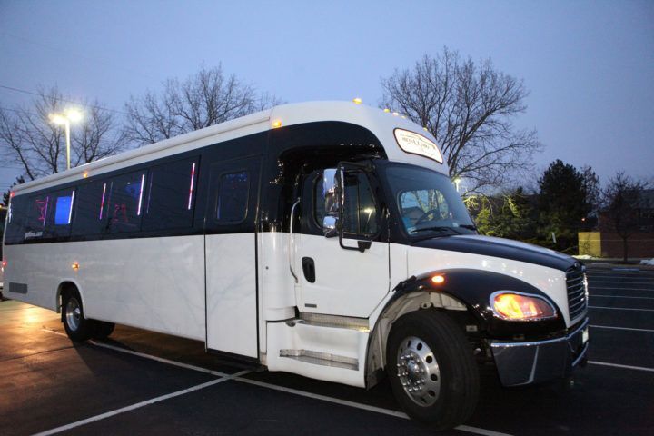 White shuttle bus parked at dusk with headlights on in a wet parking lot