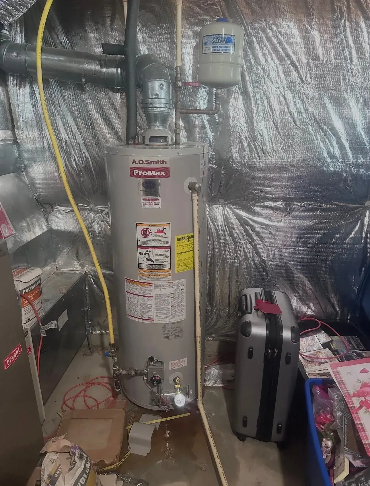 Water heater in a basement utility area with foil insulation and a tool case on the floor.