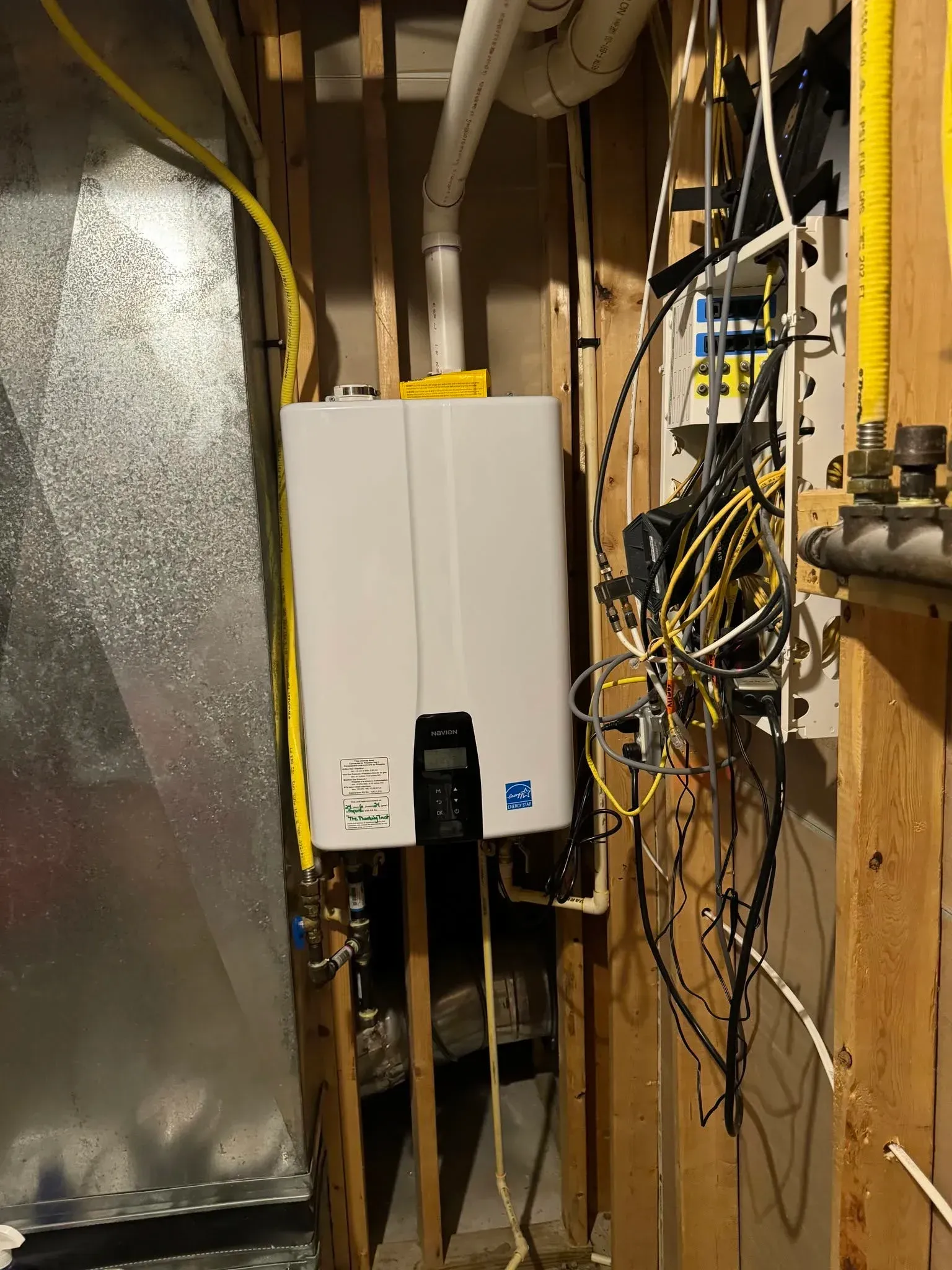 Basement utility wall with white electrical panel, exposed wiring, and metal ducting.