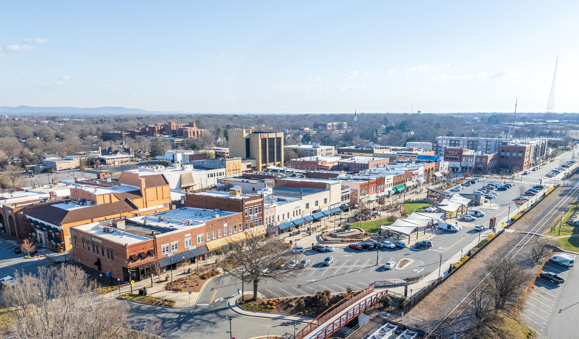 Aerial view of a small town center with historic brick buildings, a parking lot, and adjacent railroad tracks.
