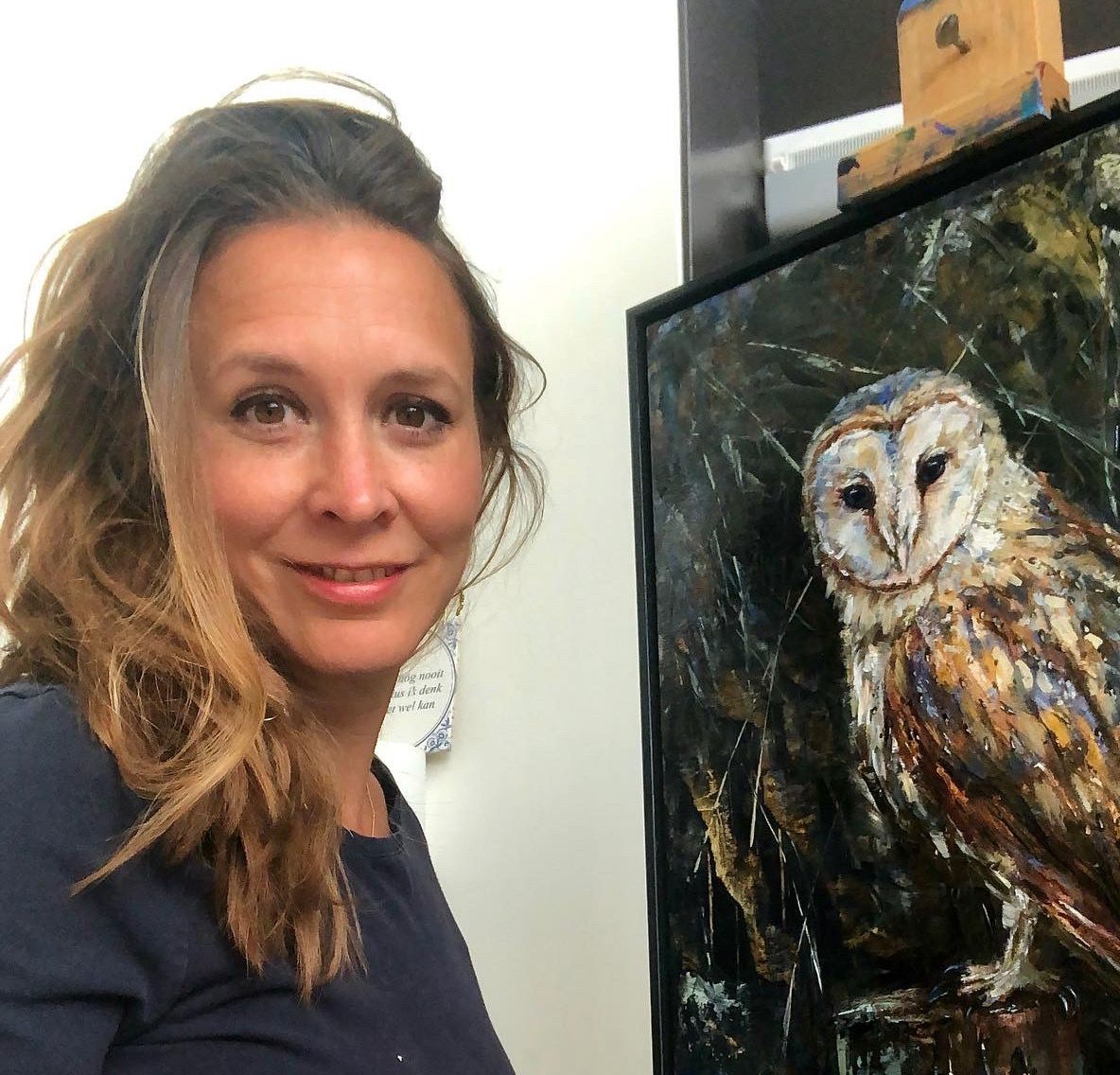 Woman smiling beside a framed owl painting with dark and warm tones.