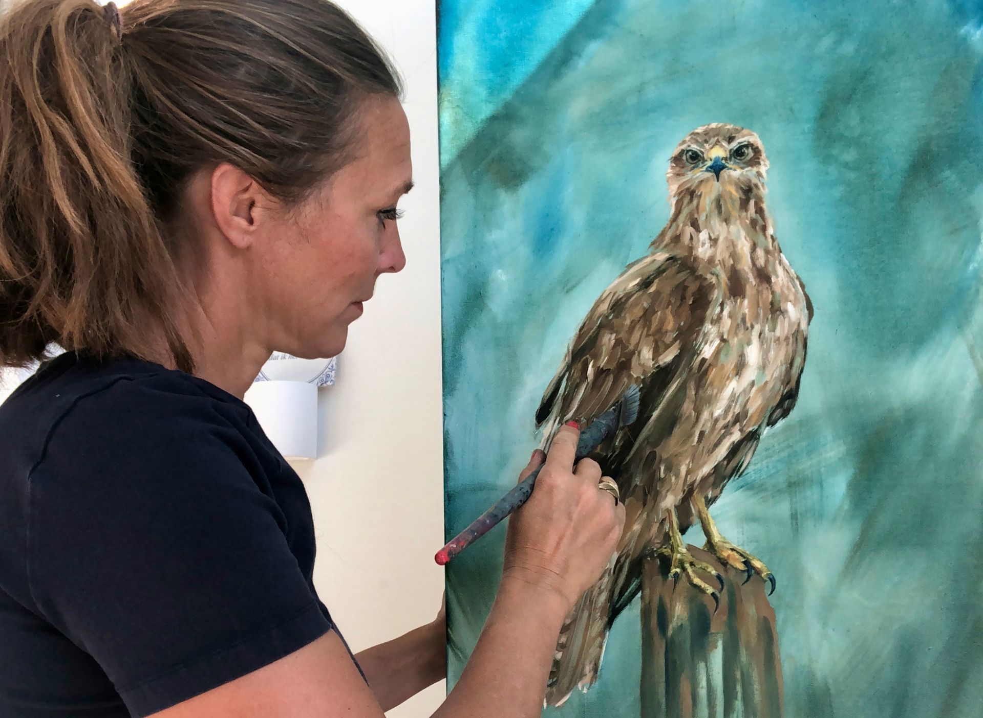 Woman painting a brown hawk on a blue and green canvas.