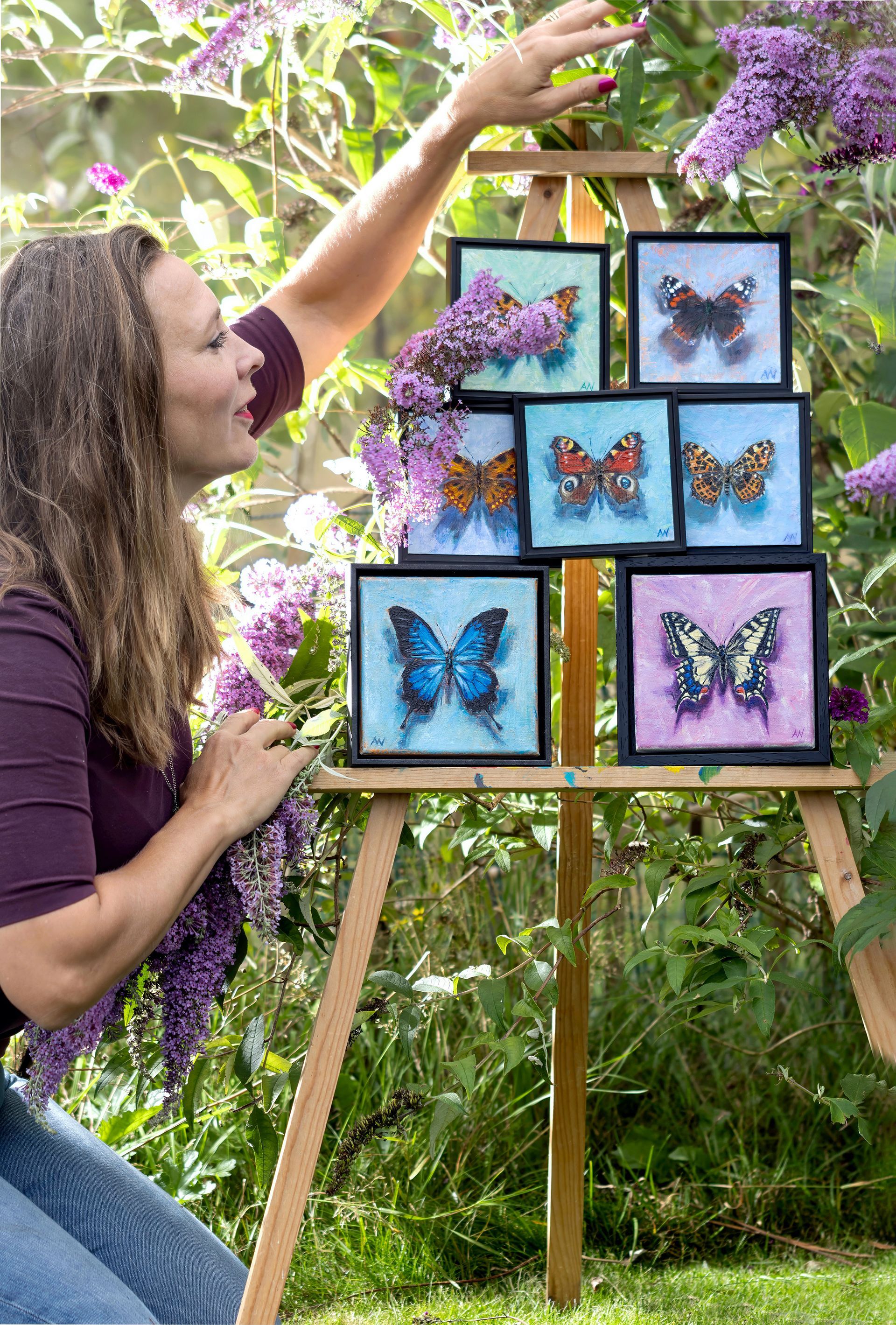 Woman reaching toward paintings of butterflies displayed on an easel outdoors.