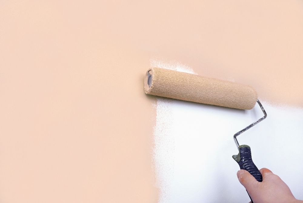 Hand painting wall with paint roller; peach wall being painted white.