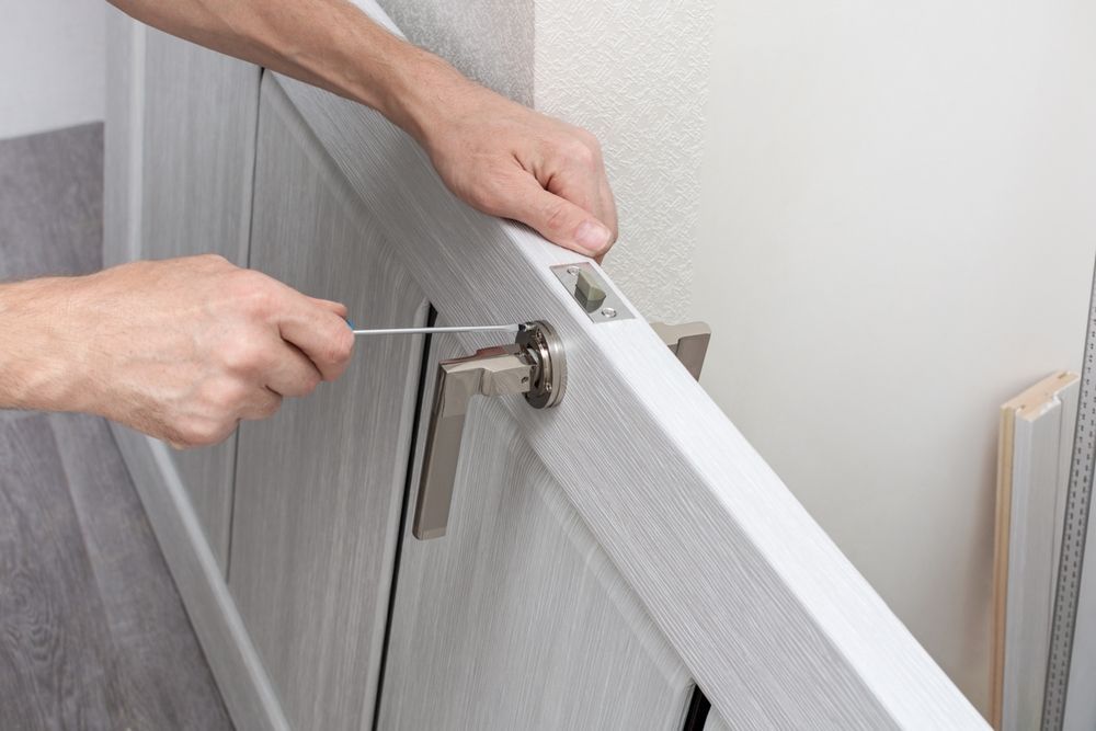 Person using a screwdriver to install door hardware on a white door.