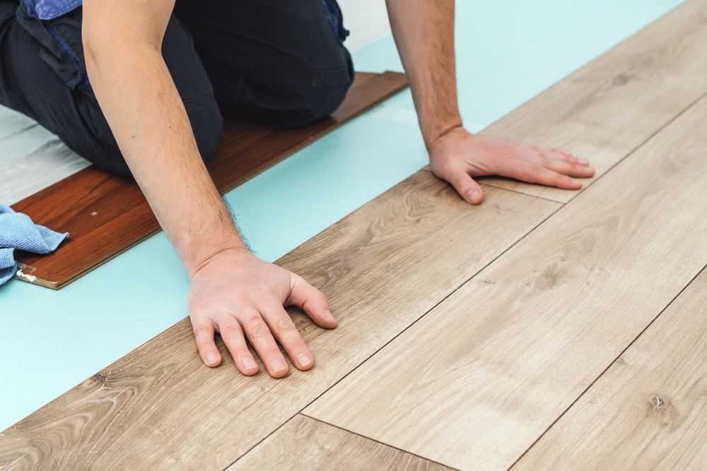 Person installing laminate flooring, kneeling, with hands on planks.