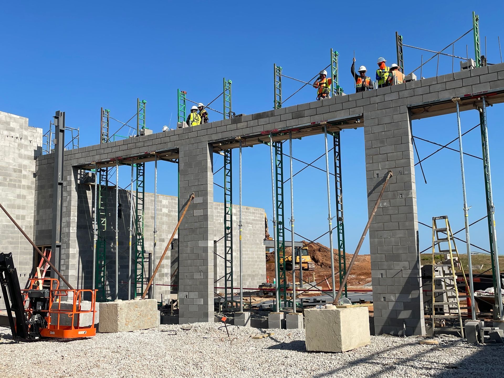 Construction crew on steel-framed building under construction, with scaffolding and equipment on site.