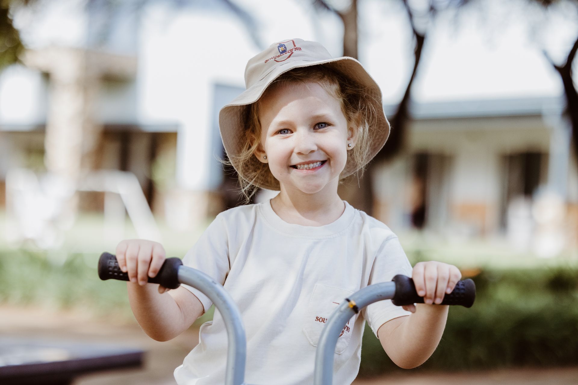 A little girl wearing a hat is riding a bike in a park.