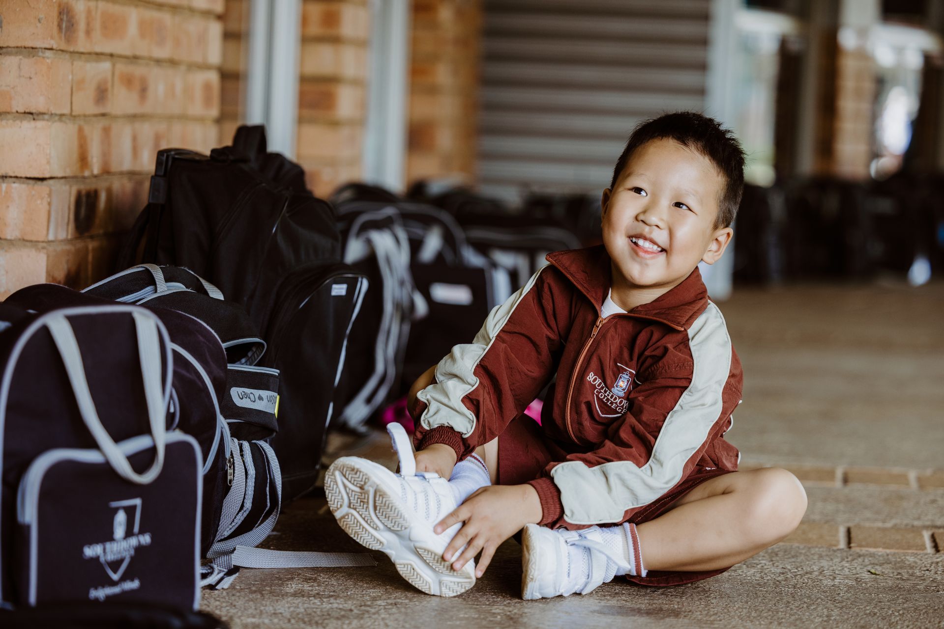 A young boy is sitting on the ground next to a pile of bags.