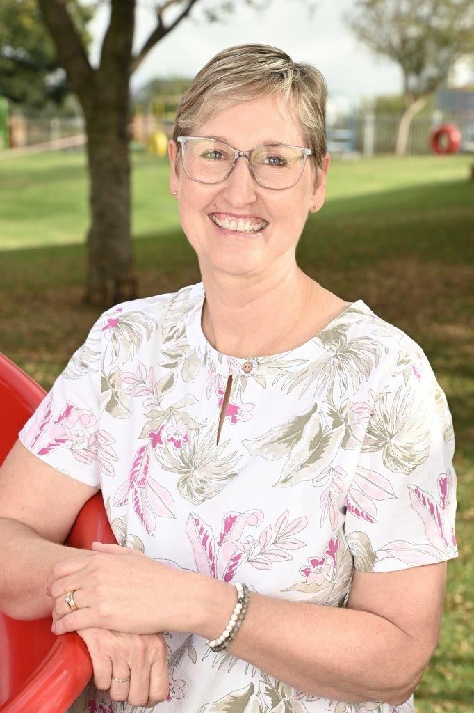 A woman wearing glasses is leaning on a red slide in a park.