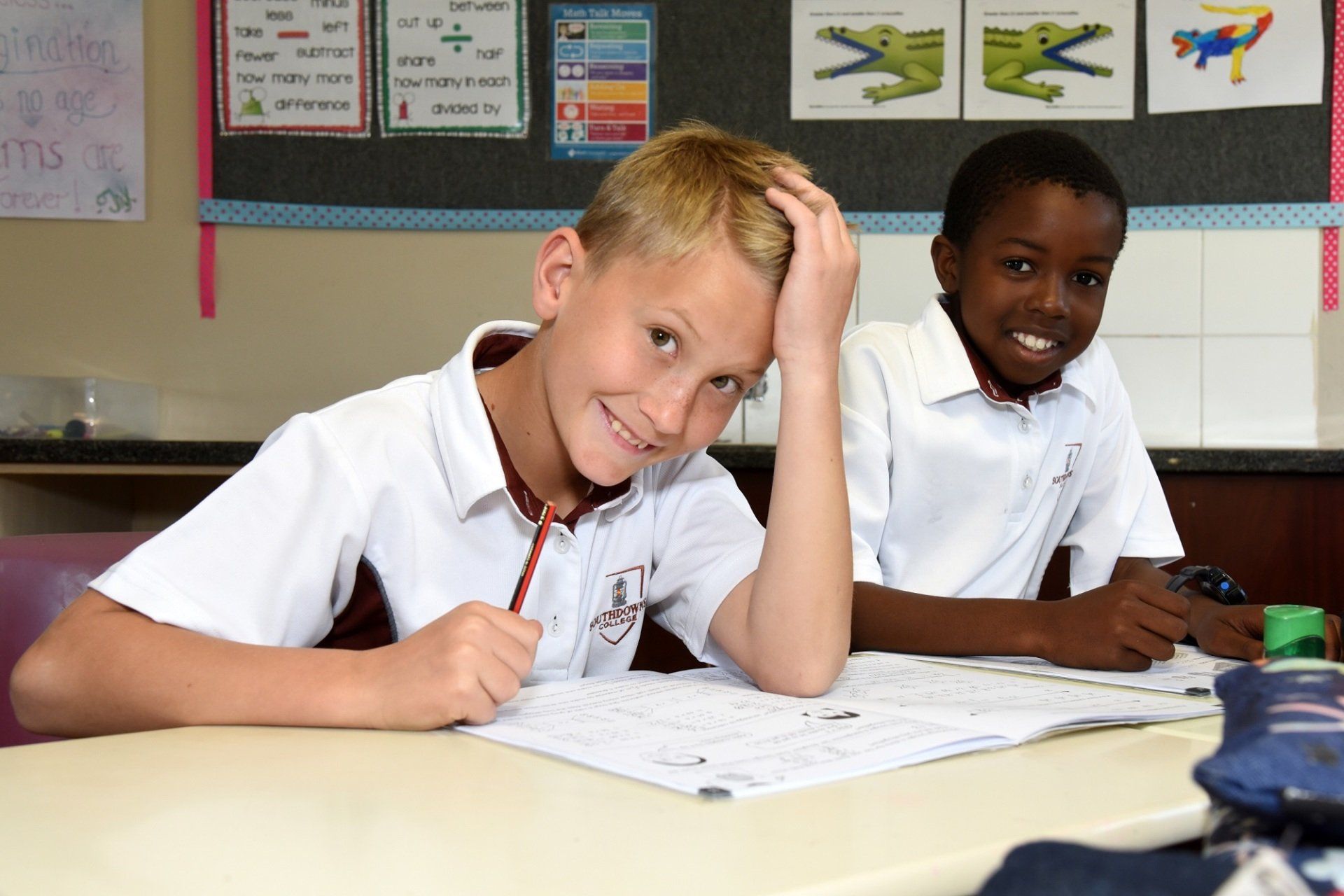 Two young boys are sitting at a desk in a classroom.