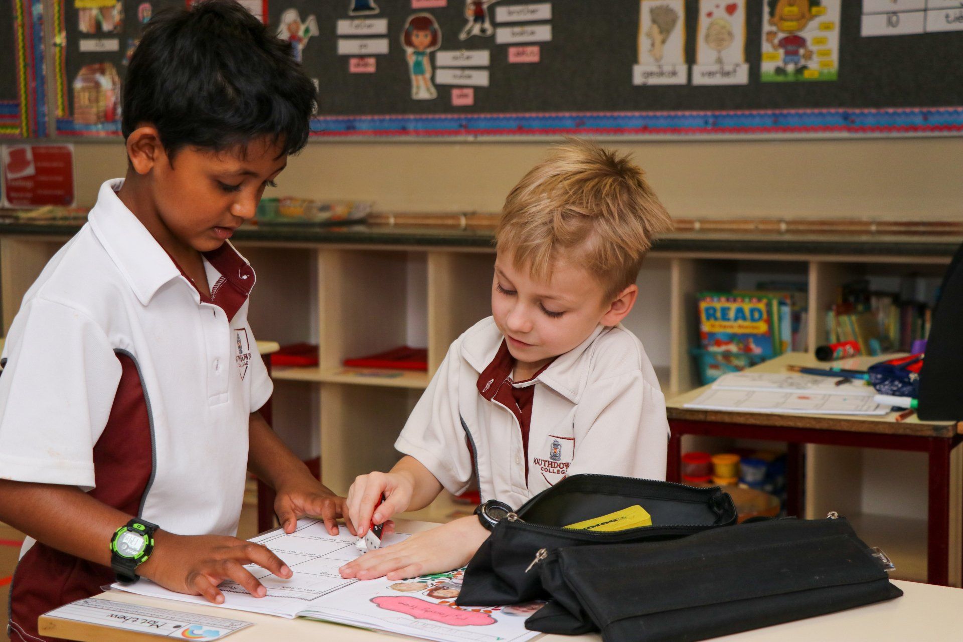 Two young boys are looking at a book together in a classroom.