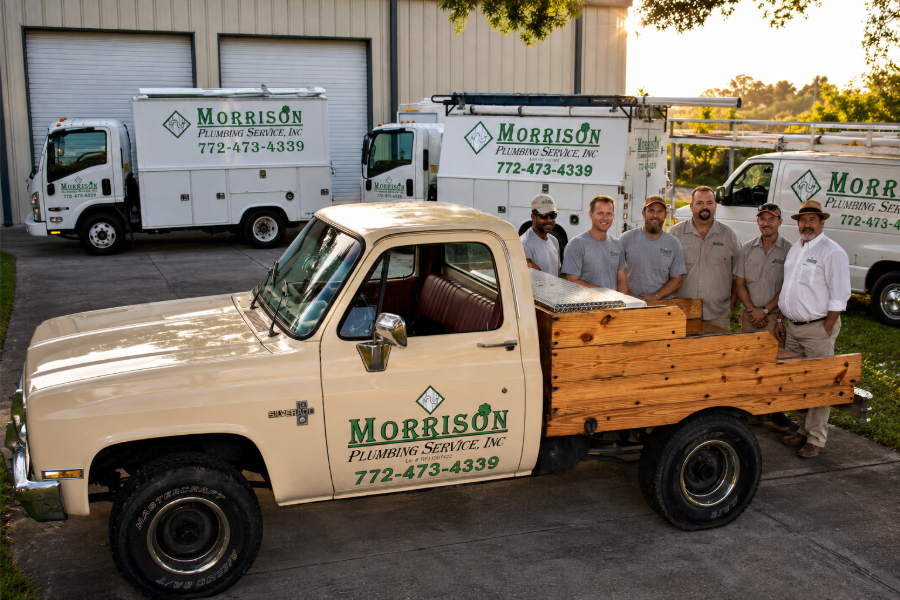 Morrison’s moving truck and crew beside white trucks in a driveway at sunset