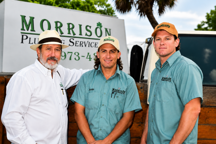 Three men in work uniforms standing before a Morrison Plumbing Services sign.