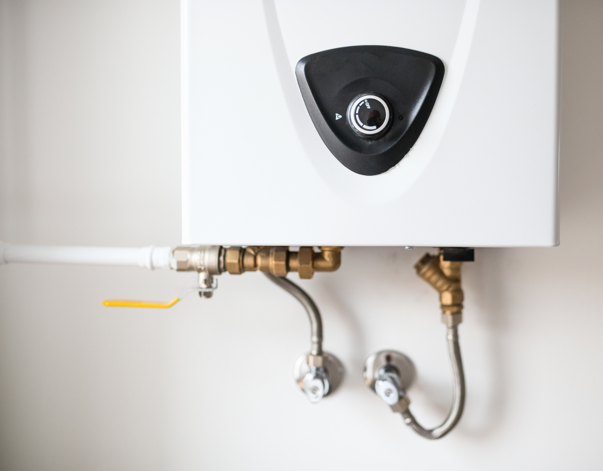 White wall-mounted water heater with exposed pipes and valves beneath it