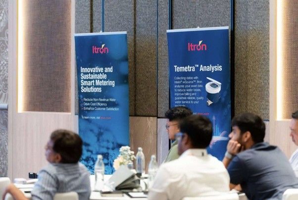 Audience seated at a conference with blue Itron banners and presentation materials