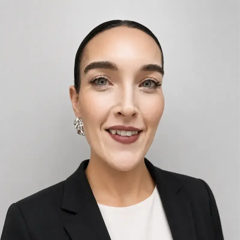 Woman in a black blazer and white top, smiling against a plain light gray background.