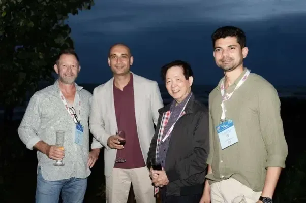 Four people standing together at an evening event, wearing conference badges and holding drinks.