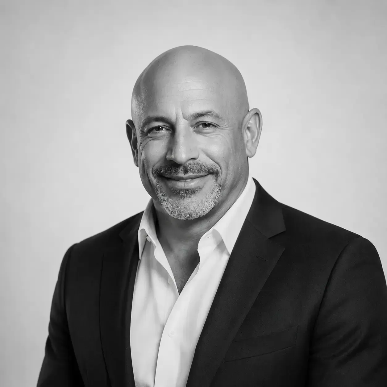 Smiling bald man in a dark suit and white shirt against a gray background