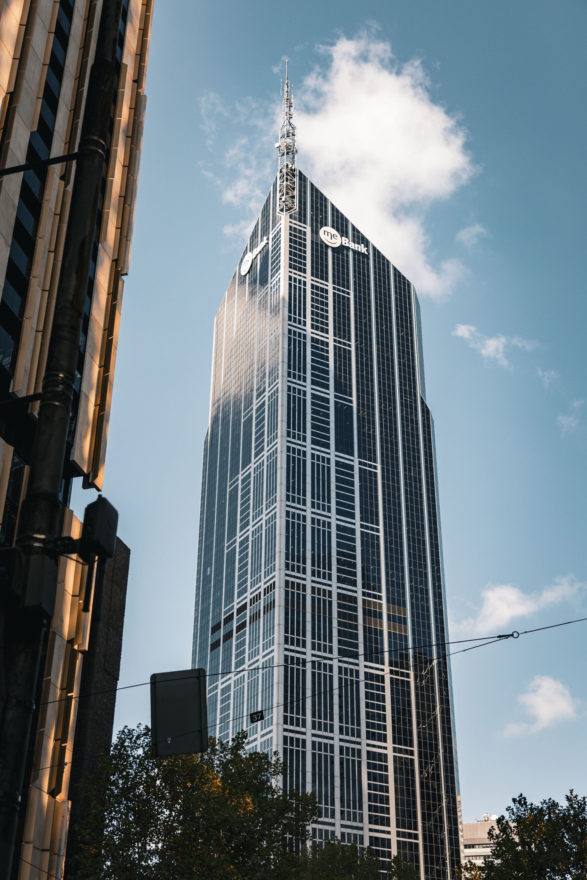 Tall glass skyscraper with a pointed top against a blue sky and clouds