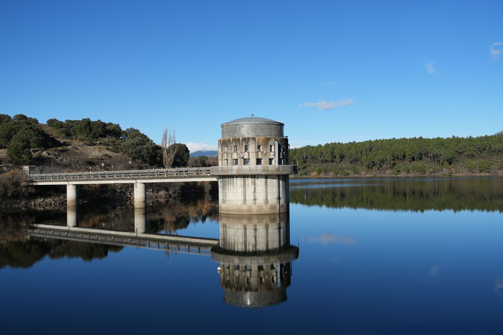 Stone tower and bridge reflected in calm water under a clear blue sky.
