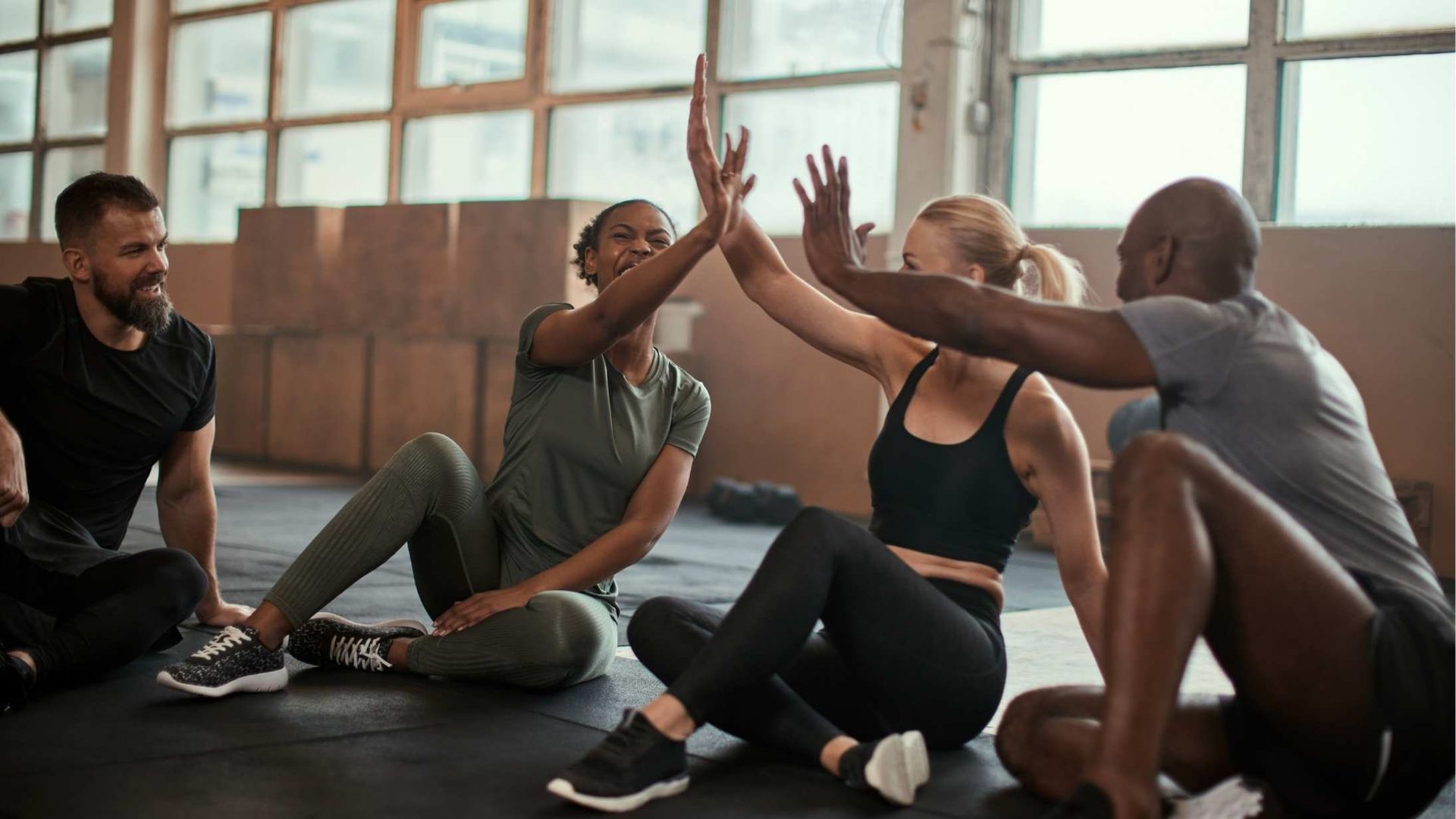Group of diverse people in workout gear high-fiving each other in a gym setting.