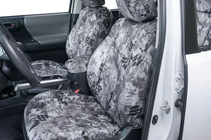 The front seats of a white car with camouflage seat covers.
