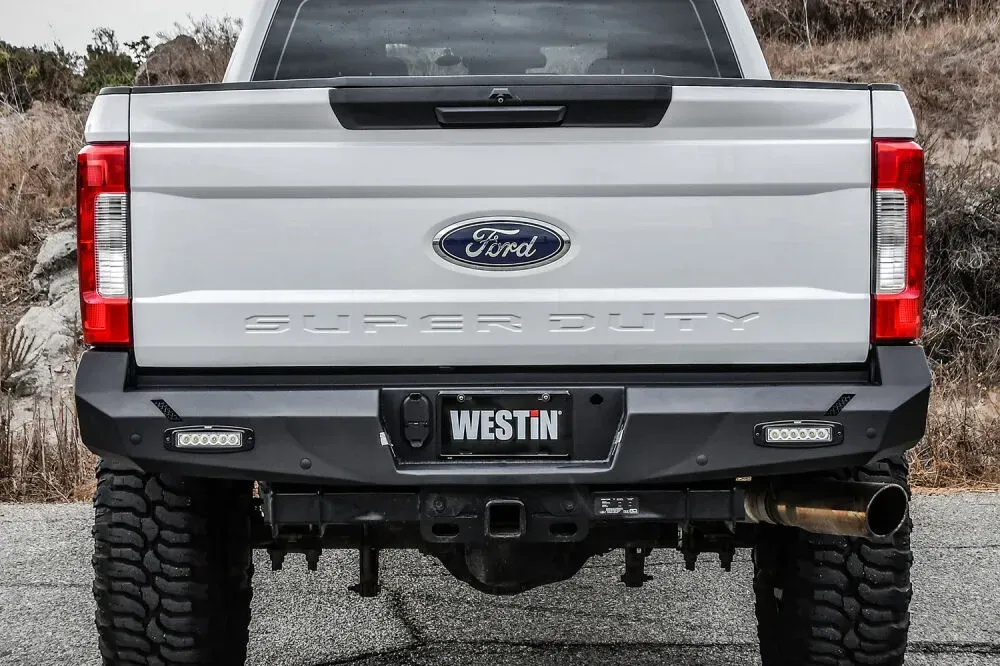 A white ford super duty truck with a black bumper is parked on the side of the road.