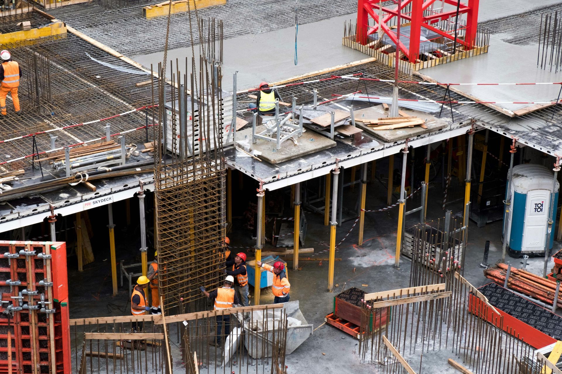 Construction workers in safety gear assemble rebar and concrete formwork at a building site from an aerial perspective.