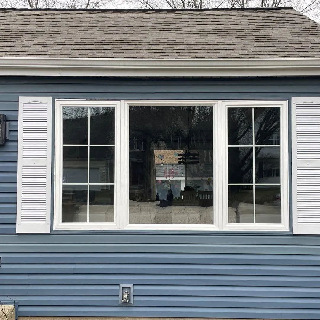 Blue house exterior with large white-trimmed windows and shutters under a shingled roof.