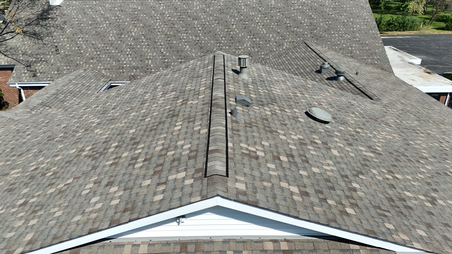 Overhead view of a house roof covered in brown and gray shingles with vents and a ridge cap.