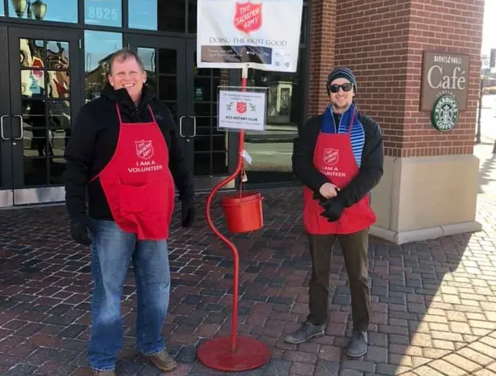 Two people wearing red Salvation Army aprons stand by a donation bucket outside a Starbucks cafe.