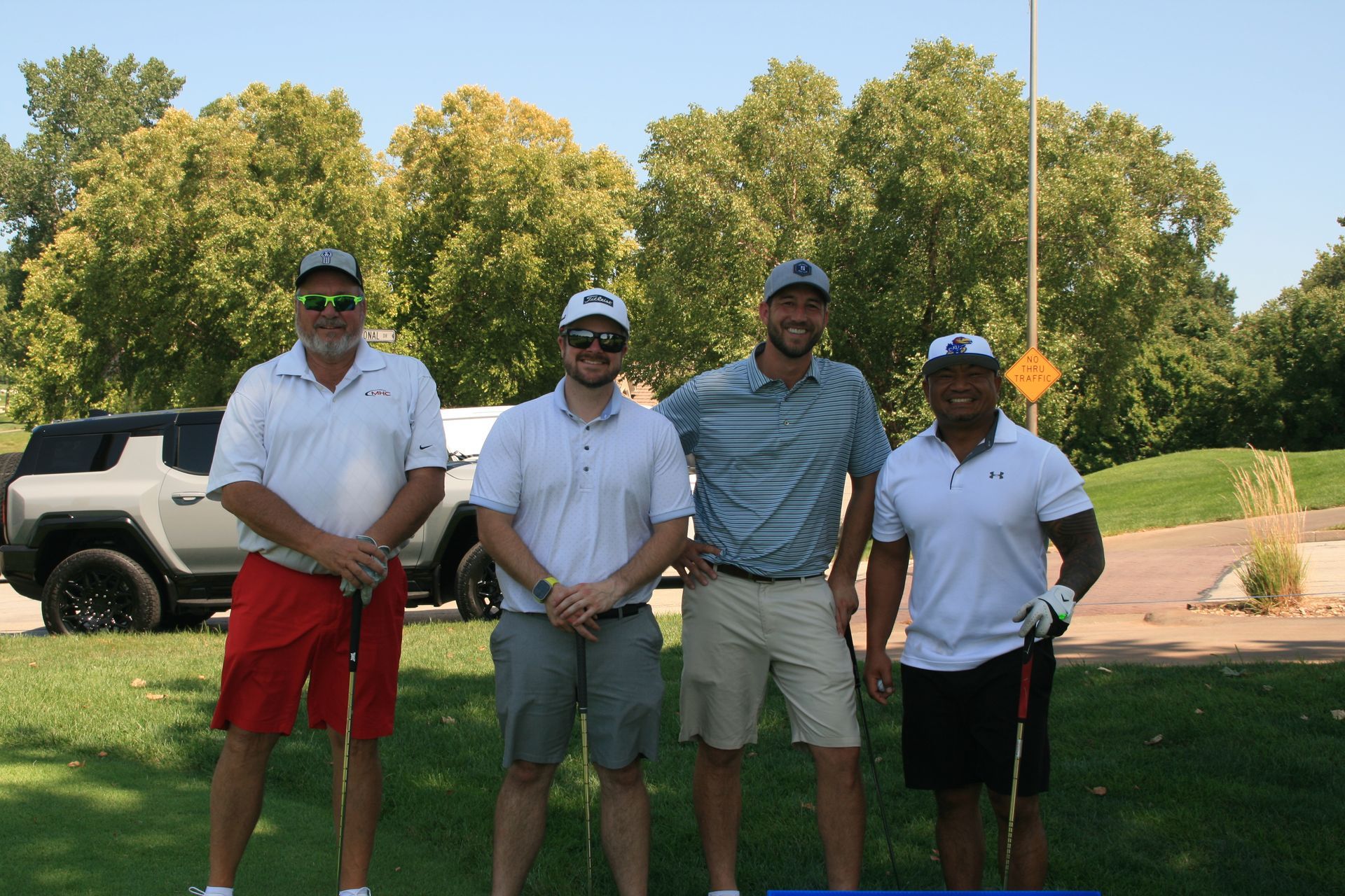 Four men on a golf course pose for a photo, with a Hummer in the background.