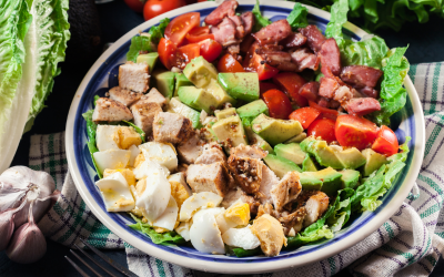 Colorful salad bowl with avocado, tomatoes, bacon, eggs, croutons, and greens on a table