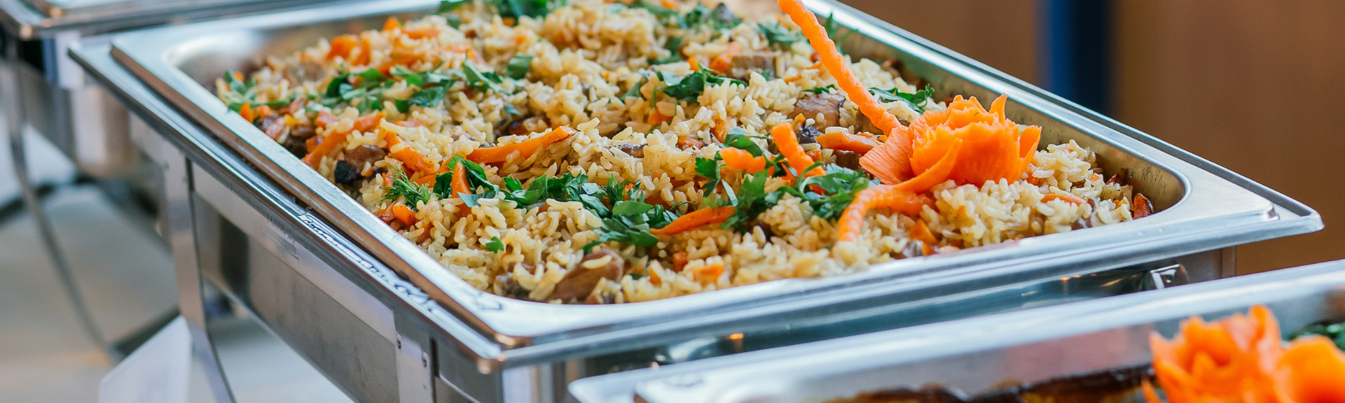Trays of rice and vegetables in a stainless-steel buffet warmer with serving tongs