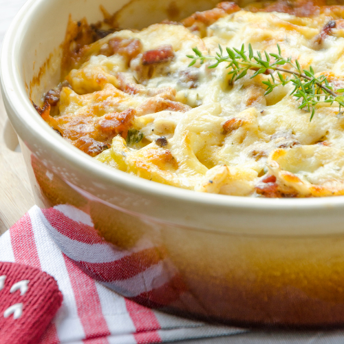 Baked cheesy casserole in a white dish, topped with herbs and browned spots, beside a red striped cloth