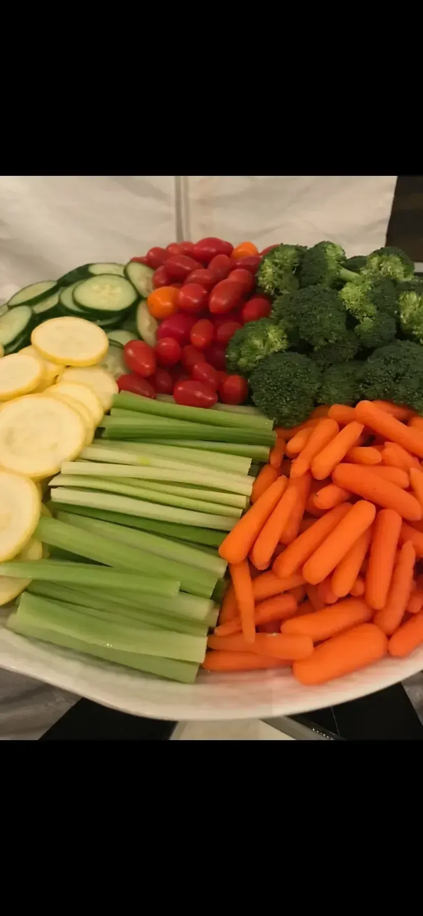 Assorted fresh vegetables arranged on a plate: zucchini, cherry tomatoes, broccoli, carrots, and celery.