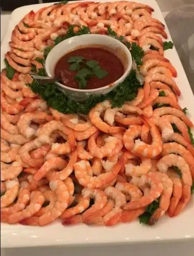 Shrimp ring arranged on a platter around a bowl of red cocktail sauce, garnished with parsley