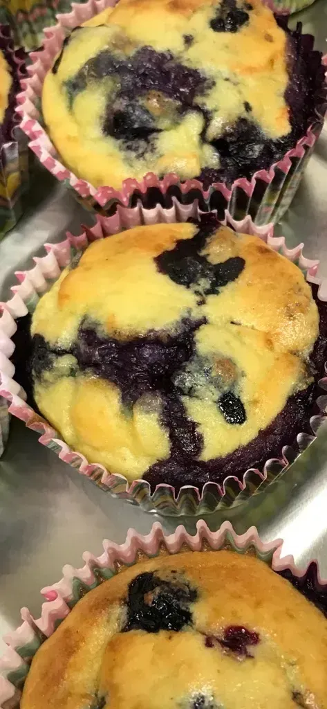 Three blueberry muffins in pink paper cups, golden tops with dark berry swirls.