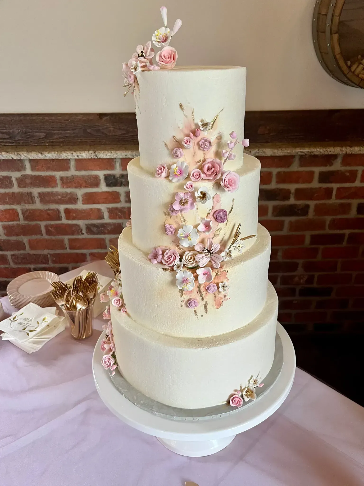 Tall white tiered wedding cake with pink floral decorations and gold accents on a display table