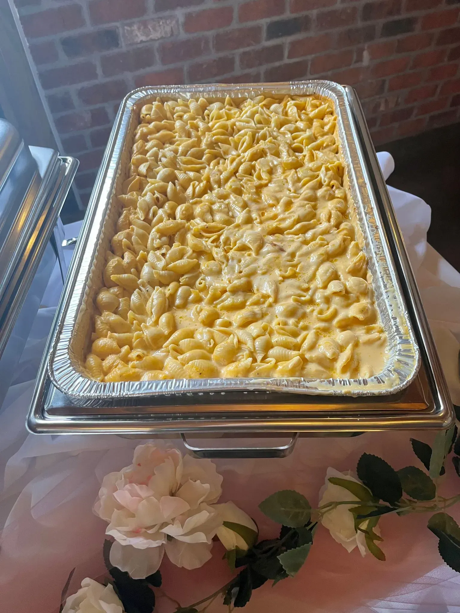 Tray of creamy baked macaroni and cheese at a buffet, garnished with parsley and surrounded by flowers
