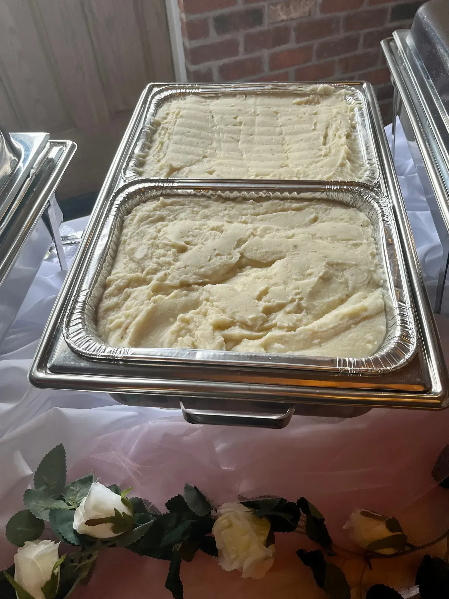 Chafing dishes filled with mashed potatoes at a buffet, with floral garland on the tablefront.