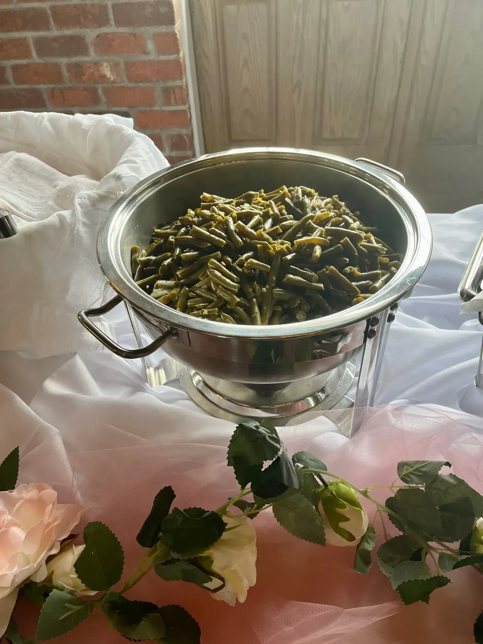 Silver pot of cooked green beans on a white tablecloth with green and white floral decor