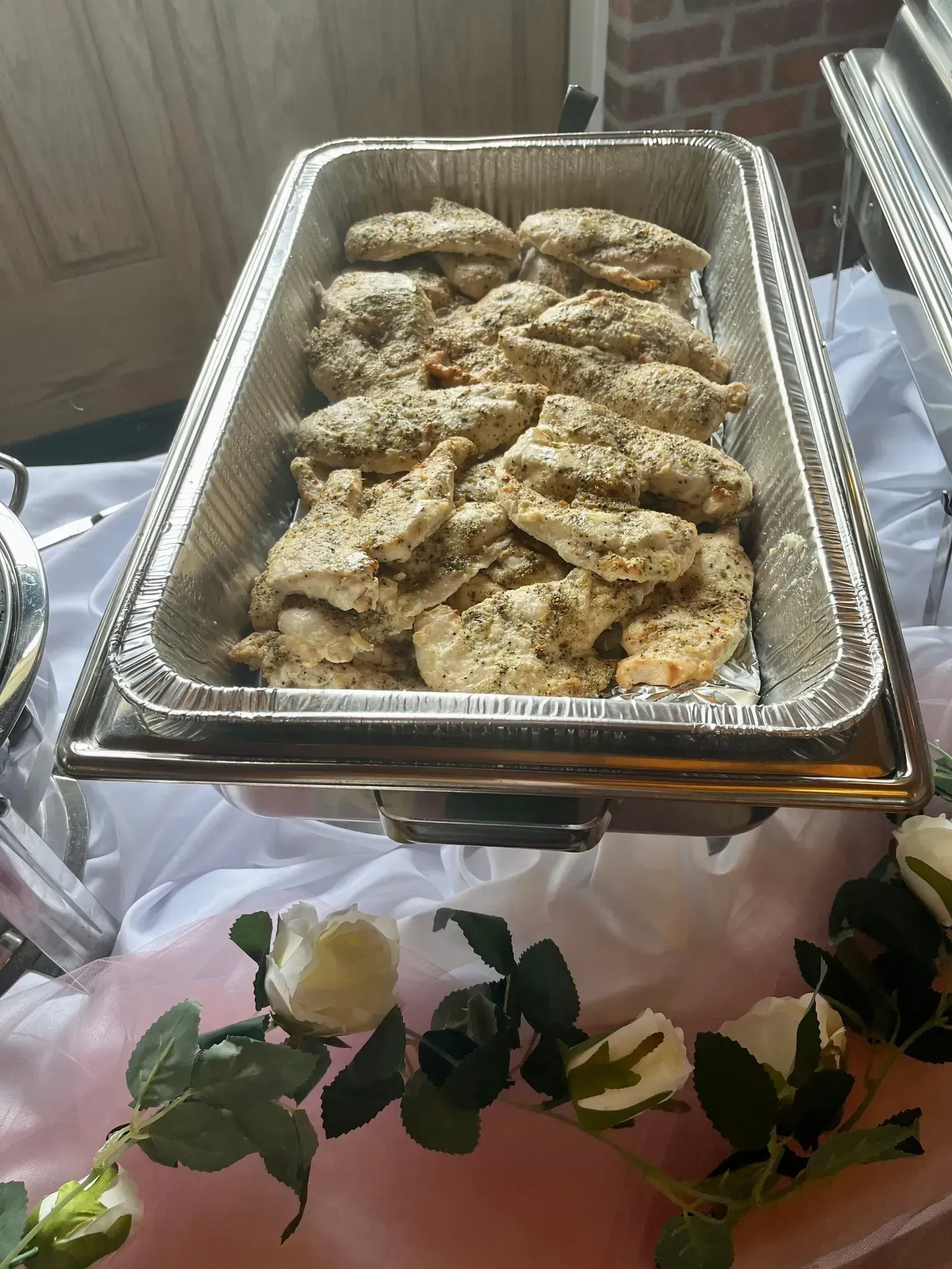 Tray of breaded baked pieces at a buffet table with floral decoration underneath