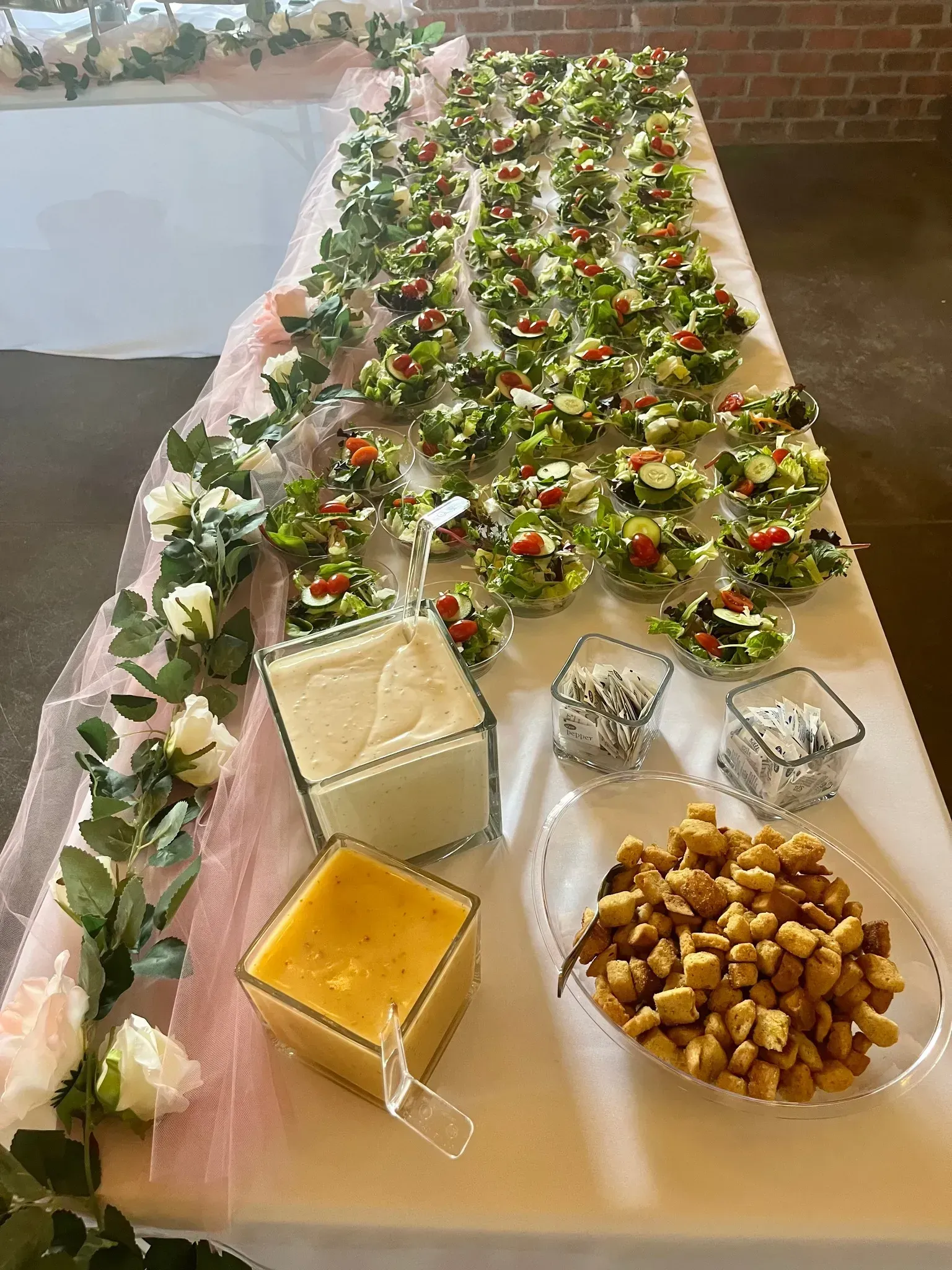 Decorated buffet table with desserts, fruit, and a green floral garland centerpiece outdoors