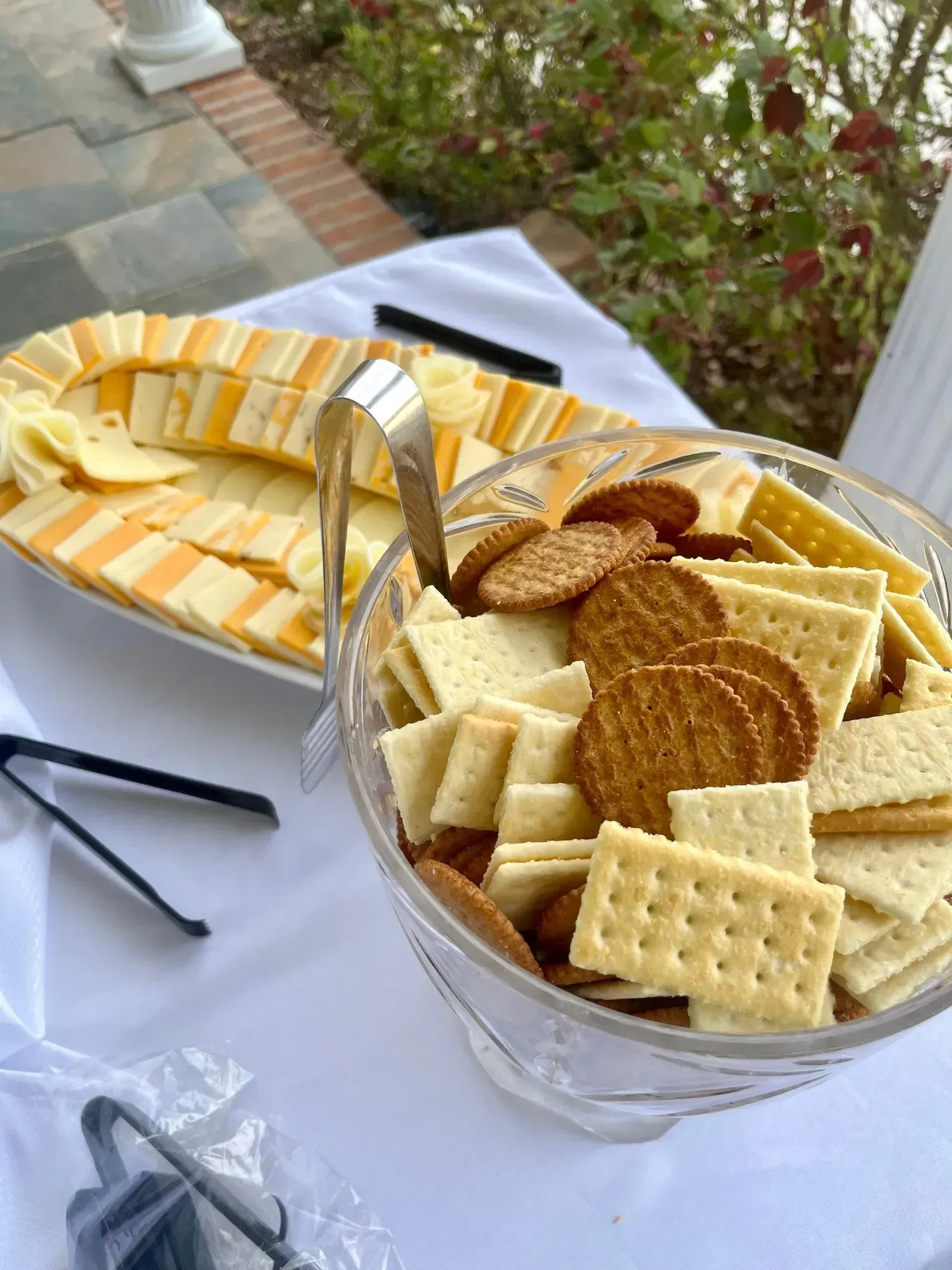 Assorted crackers and sliced cheese arranged on platters on an outdoor table
